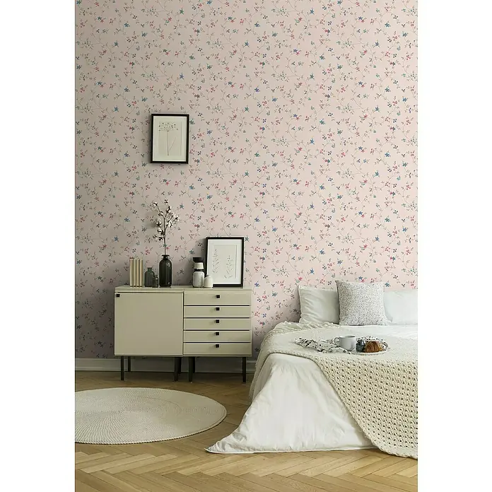 A.S. Création Maison Charme Vliestapete Blümchenranke - Creme-Grün-Blau, Floral, 10,05 x 0,53 m - Schlafzimmer mit blumiger Tapete, Kommode mit Deko, rundem Teppich und einem gemütlichen Bett mit Kissen und Tagesdecke.