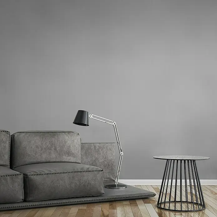 A.S. Création Maison Charme Vliestapete - Mittelgrau, Uni, 10,05 x 0,53 m - Graues modulares Sofa mit Stehlampe und rundem Beistelltisch aus Metall, die eine moderne und minimalistische Wohnraumästhetik schaffen.