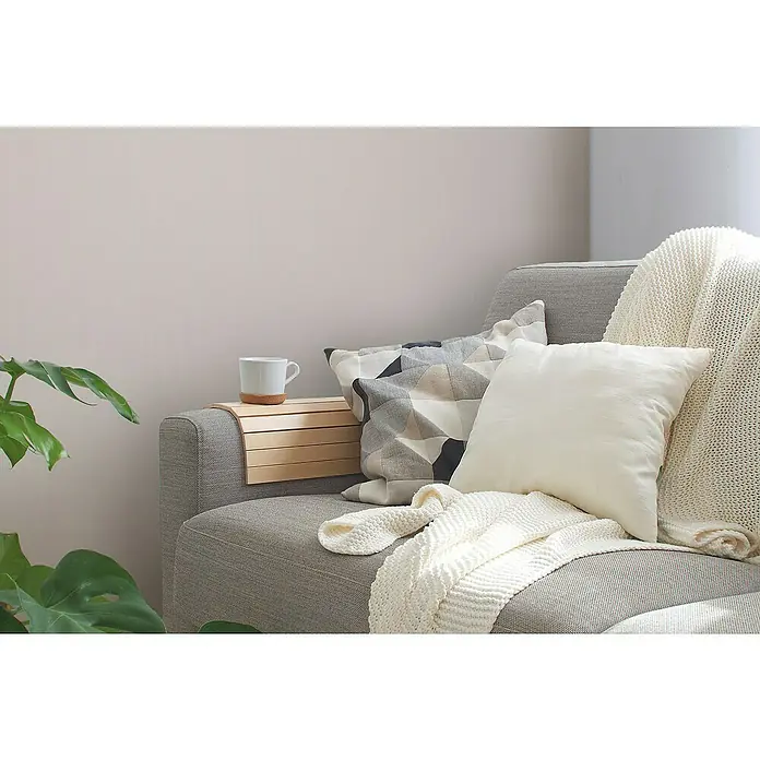 A.S. Création Maison Charme Vliestapete - Creme, Uni, 10,05 x 0,53 m - Gemütliche Sofaecke mit einer hellen Strickdecke, Zierkissen und einem Getränkehalter. Eine Tasse steht bereit für entspannte Stunden.