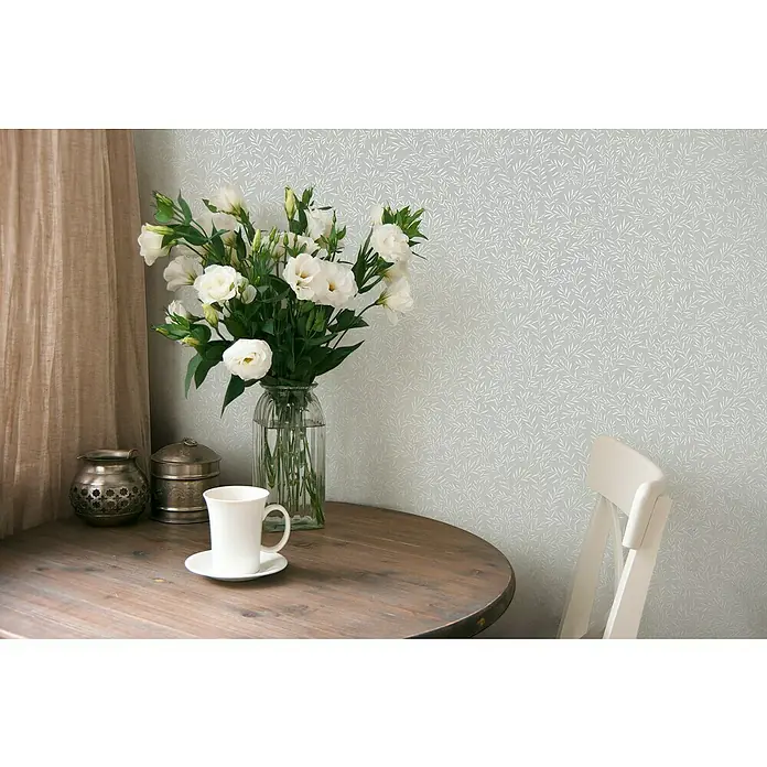 A.S. Création Maison Charme Vliestapete Ranken - Grau-Weiß, Floral, 10,05 x 0,53 m - Stillleben mit einer Tasse und Blumen auf einem Holztisch, dekoriert mit antikem Geschirr vor einer zarten floralen Tapete.