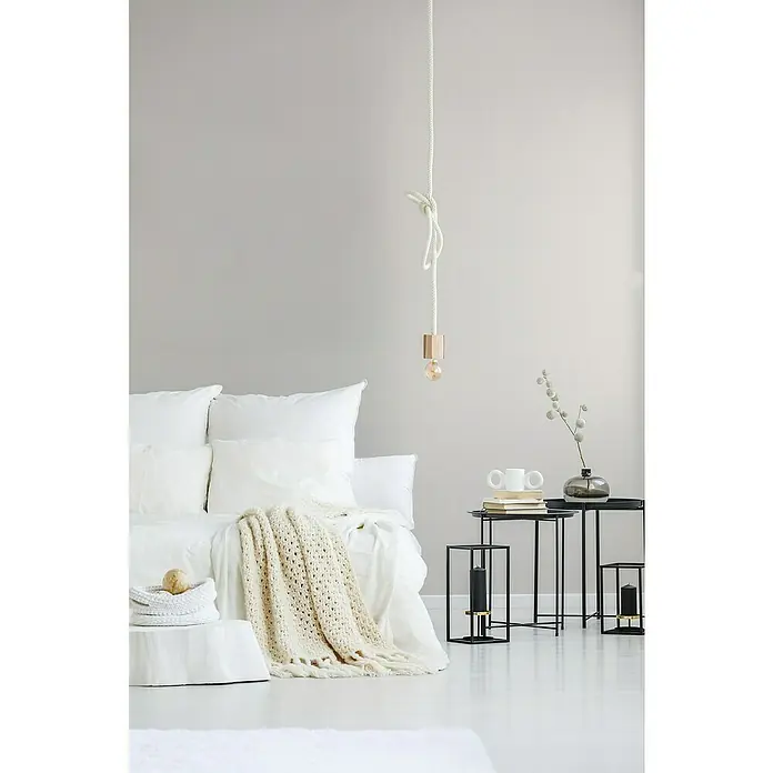 A.S. Création Maison Charme Vliestapete - Creme-Grau, Uni, 10,05 x 0,53 m - Ein minimalistisches Schlafzimmer mit einem weißen Bett, einer Strickdecke und einer hängenden Glühbirne an einem Seil, das für eine gemütliche Atmosphäre sorgt.