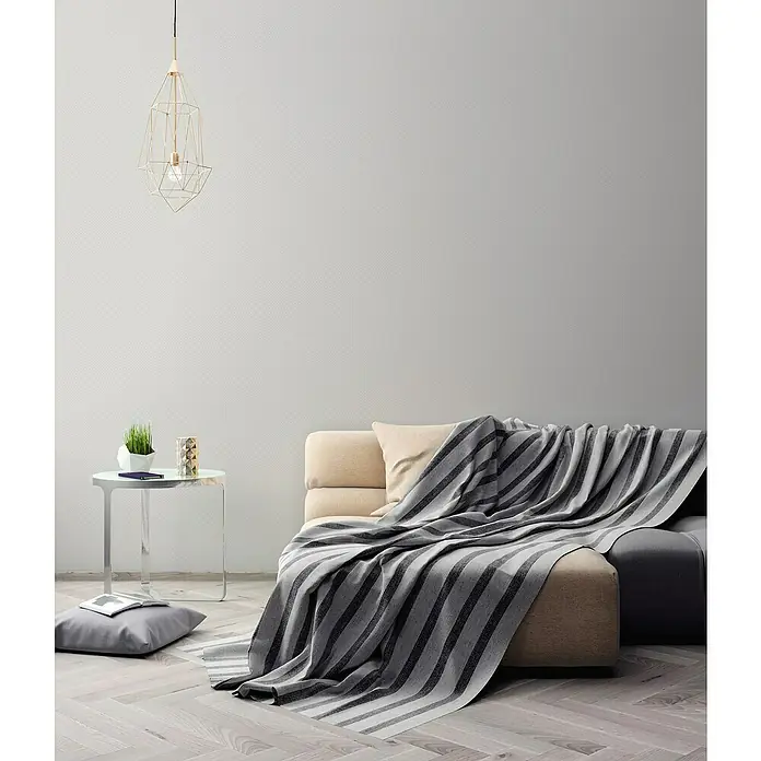A.S. Création Maison Charme Vliestapete Punkte - Grau-Weiß, Grafisch, 10,05 x 0,53 m - Wohnzimmer-Szene mit einer gestreiften Tagesdecke auf dem Sofa, einer Lampe und einem Beistelltisch, die eine gemütliche Atmosphäre schaffen.