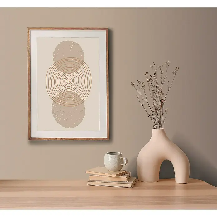 A.S. Création Pintwalls 2 Vliestapete - Braun-Beige, Uni, 10,05 x 0,53 m - Gerahmtes, abstraktes Kunstwerk mit beigen Kreisen, neben einer stilvollen Vase mit Trockenblumen und einer Tasse auf Büchern, die eine ruhige Ästhetik bieten.