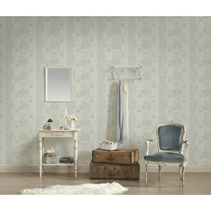 A.S. Création Maison Charme Vliestapete Blümchen-Collage - Blau-Grau-Weiß, Floral, 10,05 x 0,53 m - Dekoratives Interieur mit einem weißen Beistelltisch, alten Koffern, einem Spiegel, einer Garderobe und einem blauen Sessel vor einer gemusterten Tapete.