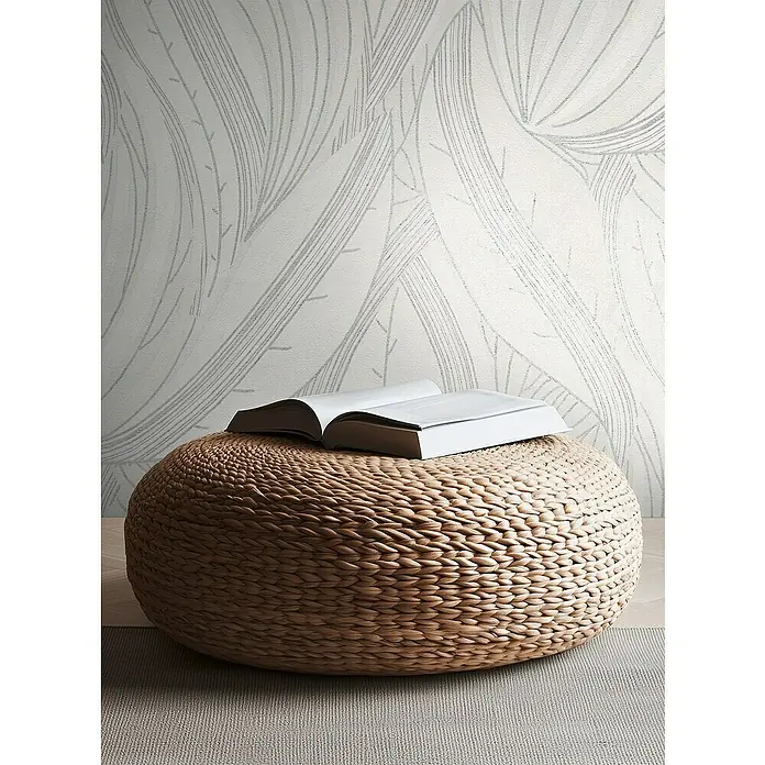 A.S. Création Metropolitan Stories Hot Spots Vliestapete Floral - Weiß-Hellgrau-Silber, Floral, 10,05 x 0,53 m - Ein geflochtener Pouf aus Wasserhyazinthe mit einem aufgeschlagenen Buch darauf, vor einer gemusterten Wand. Praktische und stilvolle Ergänzung für jedes Zuhause.