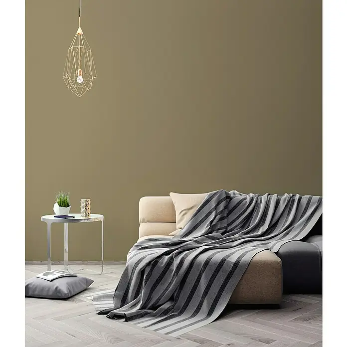 A.S. Création Pintwalls 2 Vliestapete - Grün-Khaki, Uni, 10,05 x 0,53 m - Wohnzimmer mit modernem Sofa und gestreifter Tagesdecke. Elegante Lampe und Beistelltisch ergänzen das stilvolle Interieur.