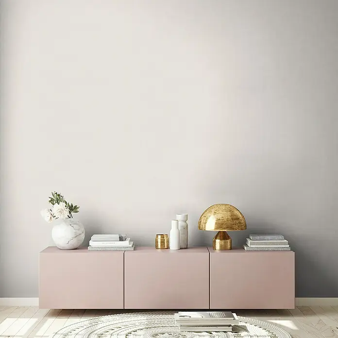 A.S. Création Maison Charme Vliestapete - Creme-Grau, Uni, 10,05 x 0,53 m - Elegante Kommode in zartem Rosa mit stilvollen Deko-Elementen wie Lampe, Büchern und Vase, die ein modernes Ambiente schafft.
