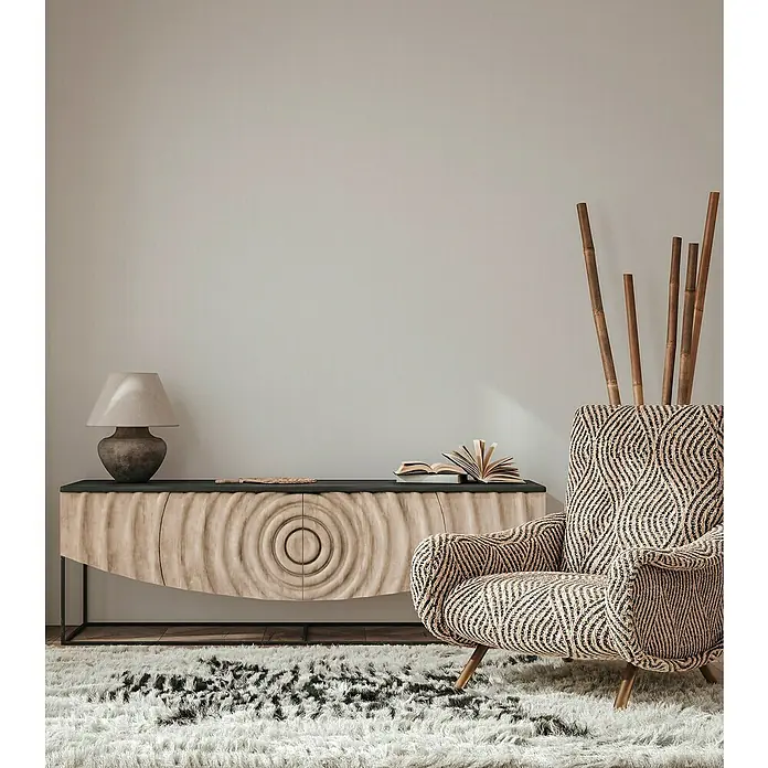 A.S. Création Maison Charme Vliestapete Kleinmuster - Hellgrau-Weiß, Uni, 10,05 x 0,53 m - Stilvolles Wohnzimmer mit einem Sideboard mit auffälligem Kreisdesign, einer Lampe, einem Buch und einem gemusterten Sessel auf einem flauschigen Teppich.