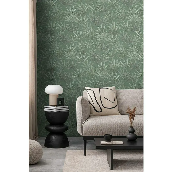 A.S. Création Michalsky Metropolis Vliestapete Hanfblätter - Grün, Floral, 10,05 x 0,53 m - Nahaufnahme eines Wohnzimmers mit einem grauen Sofa, einem schwarzen Couchtisch und einer grünen Blättertapete.