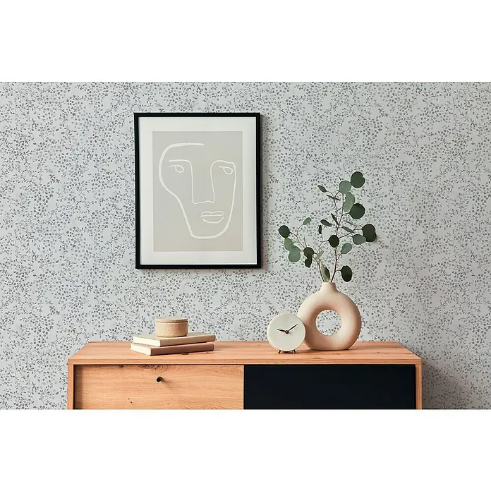A.S. Création Pintwalls 2 Vliestapete Blumen - Grau-Weiß-Silber, Floral, 10,05 x 0,53 m - Dekorative Wand mit floralem Muster, ergänzt durch ein modernes Kunstwerk und stilvolle Accessoires auf einer Holzkommode.