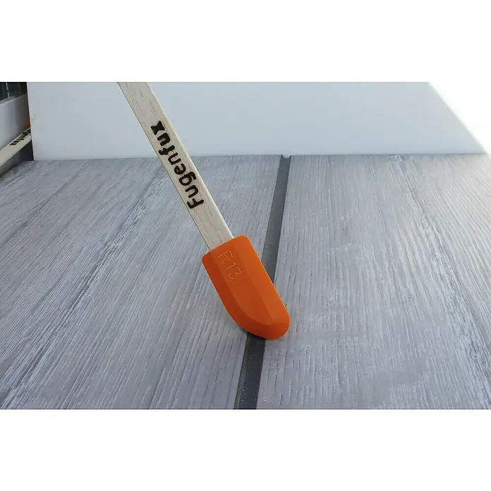 Heka Fugenglätter Fugenfux 5 in 1 - Passend für: Fugenbreite 6,3/8,3/10/13/20 mm - Nahaufnahme eines Fugenfux R13-Fugenwerkzeugs mit orangefarbenem Silikonaufsatz und Holzgriff auf einem Holztisch.