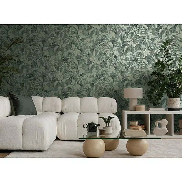 A.S. Création Metropolitan Stories Hot Spots Vliestapete Dschungel - Blau-Grün-Gold, Floral, 10,05 x 0,53 m - Wohnzimmer mit einem cremefarbenen Sofa und einem Couchtisch mit Glasplatte. Die grüne Blättertapete verleiht dem Raum eine natürliche Note.
