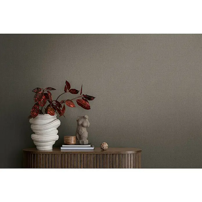 A.S. Création Michalsky Metropolis Vliestapete - Grau-Braun, Uni, 10,05 x 0,53 m - Stillleben mit skulpturaler Vase, dekorativen Büchern und einer weiblichen Torsofigur auf einer hölzernen Kommode vor einer strukturierten Wand.