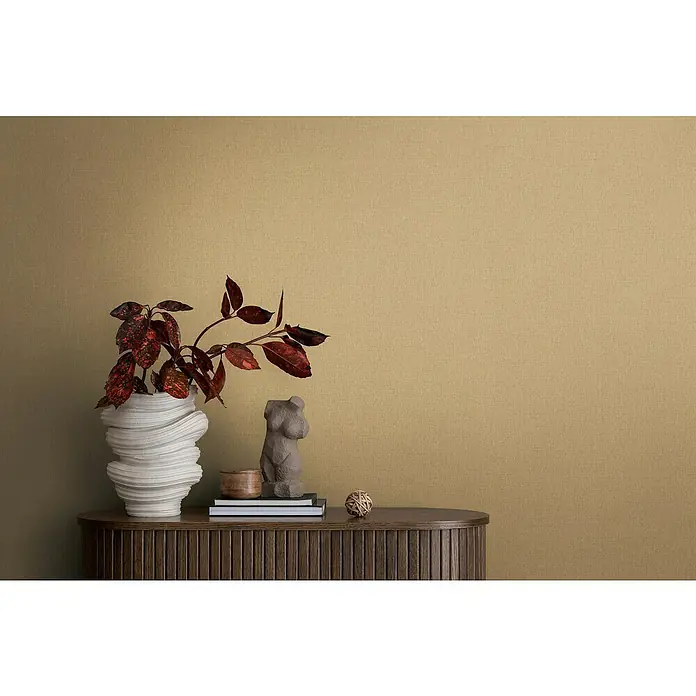 A.S. Création Michalsky Metropolis Vliestapete - Beige-Gold, Uni, 10,05 x 0,53 m - Nahaufnahme eines eleganten Sideboards mit einer kunstvollen Vase, einer Skulptur und dekorativen Elementen vor einer strukturierten Wand.