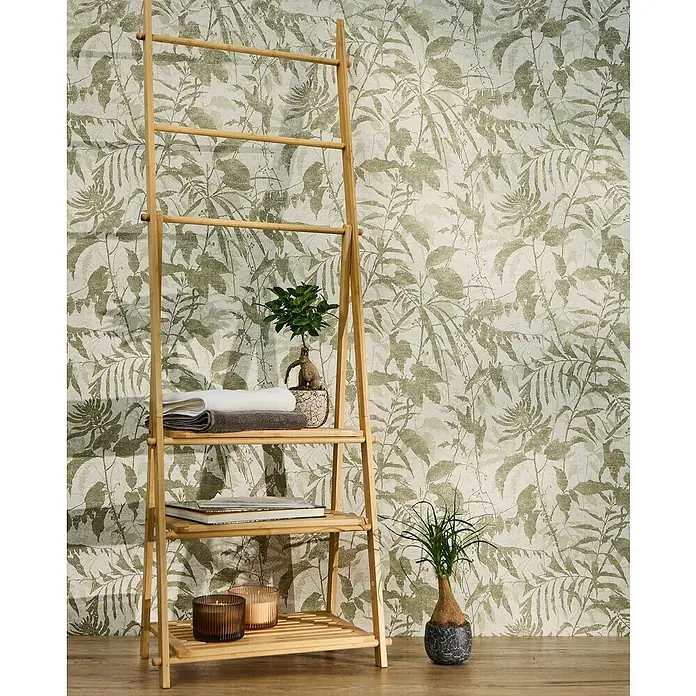 A.S. Création Metropolitan Stories Hot Spots Vliestapete Dschungel - Grün-Creme-Gold, Floral, 10,05 x 0,53 m - Das Foto zeigt ein dekoratives Holzregal mit Handtüchern, Büchern und Pflanzen vor einer gemusterten Wand.