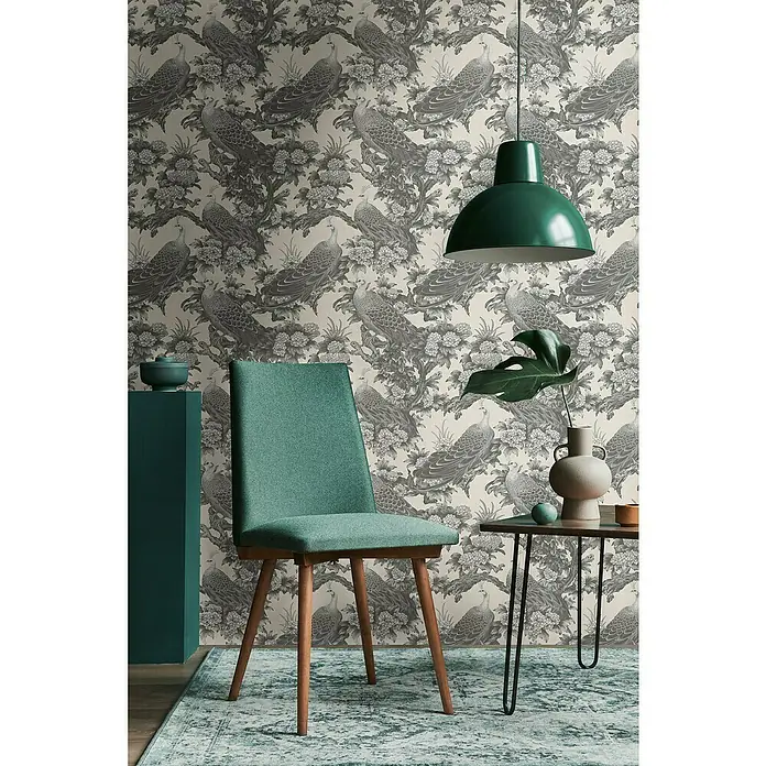 A.S. Création Michalsky Metropolis Vliestapete Dschungel - Grau-Beige, Floral, 10,05 x 0,53 m - Einrichtungsidee mit einem grünen Stuhl, einer Hängelampe und einem Beistelltisch vor einer Tapete mit Pfauenmuster für ein stilvolles Ambiente.
