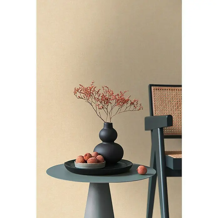 A.S. Création Metropolitan Stories Hot Spots Vliestapete - Beige-Gelb-Orange, Uni, 10,05 x 0,53 m - Nahaufnahme eines Tisches mit einer schwarzen Vase mit roten Blüten, einer Schale Lychees und einem grünen Stuhl.