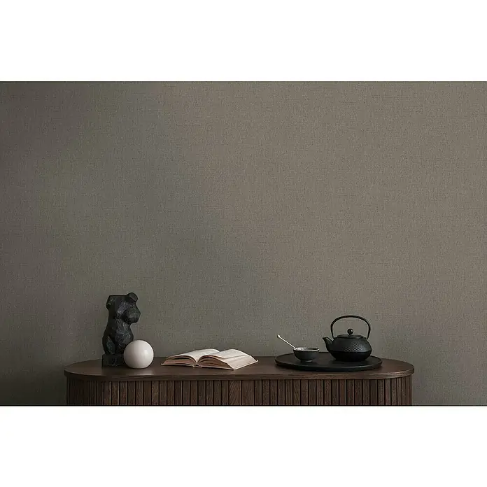 A.S. Création Michalsky Metropolis Vliestapete - Grau-Braun, Uni, 10,05 x 0,53 m - Elegantes Sideboard mit Deko-Objekten: Eine Skulptur, eine Kugel, ein offenes Buch und ein Tee-Set auf einem dunklen Holzmöbelstück.