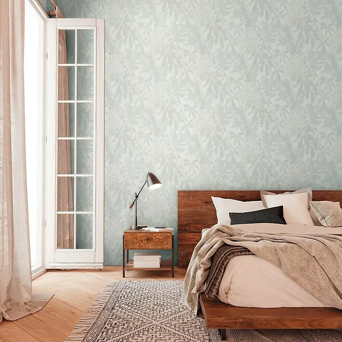 A.S. Création Daniel Hechter 7 Vliestapete Florale Schatten - Grün-Grau-Weiß, Floral, 10,05 x 0,53 m - Schlafzimmer mit einem Holzbett, Nachttisch mit Lampe und einem Teppich mit geometrischem Muster. Die Wand hat ein florales Muster.