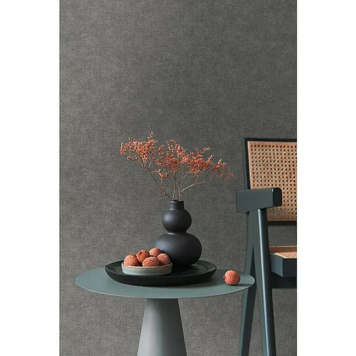 A.S. Création Metropolitan Stories Hot Spots Vliestapete - Dunkelbraun-Braun, Uni, 10,05 x 0,53 m - Nahaufnahme eines Tisches mit einer schwarzen Vase und einer Schale mit Lychees vor einer grauen Wand.