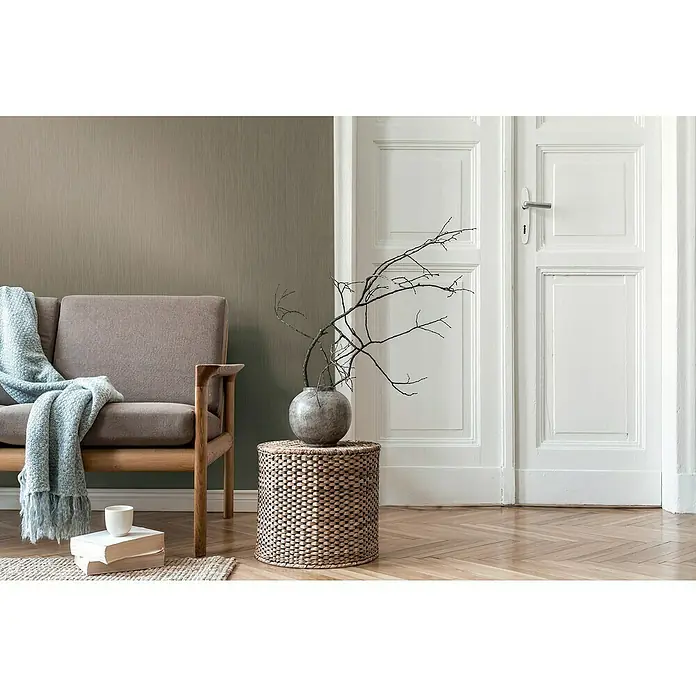 A.S. Création Daniel Hechter 7 Vliestapete - Khaki, Uni, 10,05 x 0,53 m - Ein stilvolles Interieur mit einem bequemen Sessel, einer dekorativen Vase und natürlichen Elementen, die eine harmonische Atmosphäre schaffen.