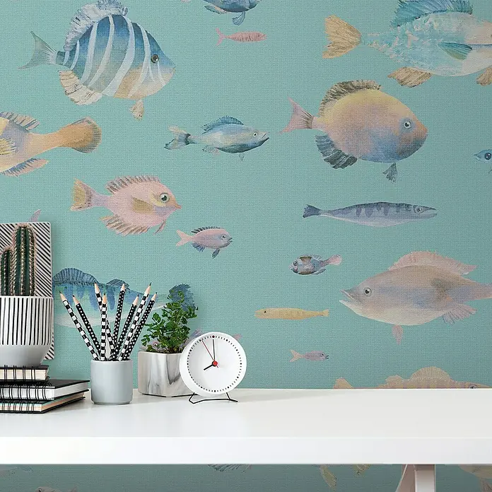 A.S. Création Pintwalls 2 Vliestapete Fische - Blau-Bunt-Violett, Tieroptik, 10,05 x 0,53 m - Eine Nahaufnahme eines Schreibtisches mit einer Uhr, Bleistiften, Pflanzen und einem Kaktus vor einer Wand mit Fischmuster.