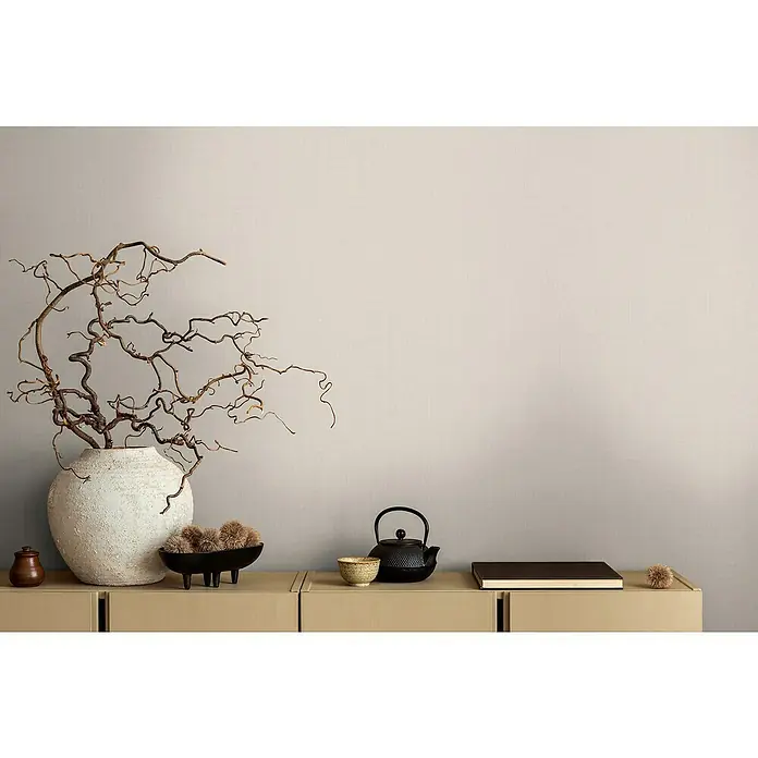 A.S. Création Michalsky Metropolis Vliestapete - Creme-Beige, Uni, 10,05 x 0,53 m - Eine beige Kommode mit einer Vase mit Ästen, einer Teekanne und einem Buch darauf.