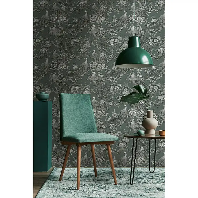 A.S. Création Michalsky Metropolis Vliestapete Dschungel - Grau-Schwarz, Floral, 10,05 x 0,53 m - Einrichtungsgegenstände mit grüner Farbgebung vor einer Tapete mit Vogelmuster, darunter ein grüner Stuhl und eine Hängelampe.