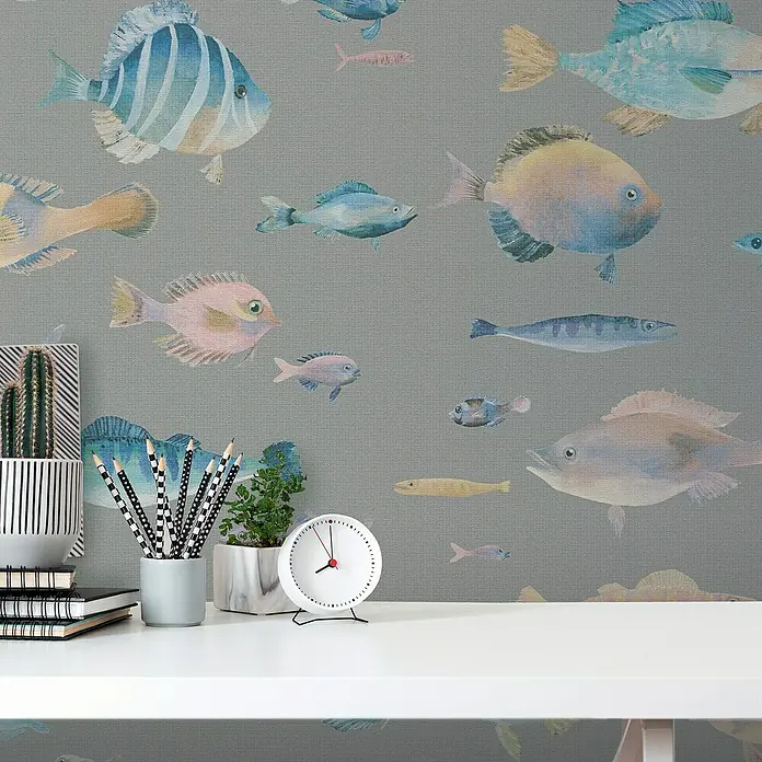 A.S. Création Pintwalls 2 Vliestapete Fische - Grau-Bunt-Blau, Tieroptik, 10,05 x 0,53 m - Schreibtisch mit Notizbüchern, Stiften, Kaktus und Uhr vor einer Tapete mit Fischmuster. Der Fokus liegt auf dem aufgeräumten Arbeitsplatz.