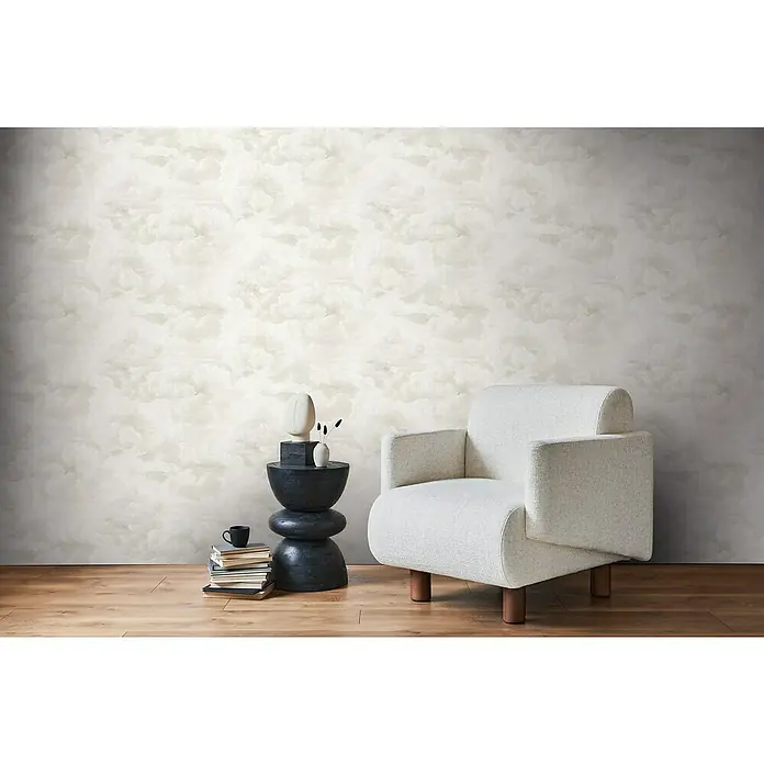A.S. Création Michalsky Metropolis Vliestapete Wolken - Creme-Weiß, Sonstiges, 10,05 x 0,53 m - Einrichtungsszene mit einem weißen Sessel, einem schwarzen Beistelltisch mit Deko und Büchern vor einer Wand mit Wolkenmuster.