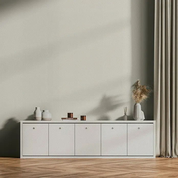 A.S. Création Daniel Hechter 7 Vliestapete 3D-Grafikstreifen - Weiß-Creme-Metallic, Grafisch, 10,05 x 0,53 m - Das Bild zeigt ein modernes Sideboard mit fünf Türen, auf dem Vasen und Dekoartikel platziert sind, vor einer schlichten Wand.