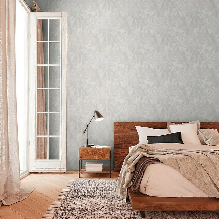 A.S. Création Daniel Hechter 7 Vliestapete Florale Schatten - Grau-Creme, Floral, 10,05 x 0,53 m - Ein Schlafzimmer mit einem gemütlichen Holzbett, Nachttischlampe und floral gemusterter Tapete für eine entspannende Atmosphäre.