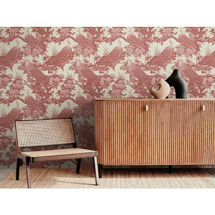 A.S. Création Michalsky Metropolis Vliestapete Dschungel - Rot-Creme-Rosa, Floral, 10,05 x 0,53 m - Ein stilvolles Zimmer mit einem Holzschrank, einem Stuhl und einer dekorativen Tapete mit Pfauenmuster.
