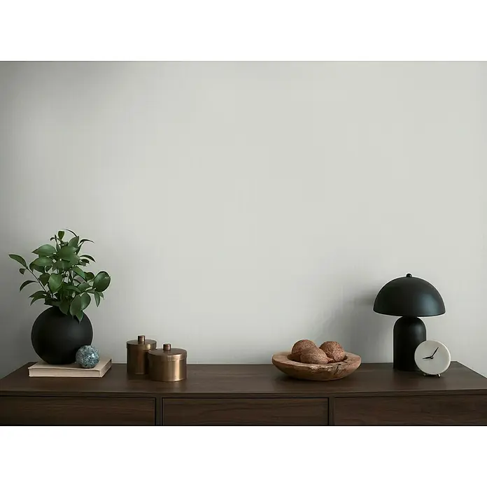 A.S. Création Michalsky Metropolis Vliestapete - Graublau, Uni, 10,05 x 0,53 m - Tischdekoration mit Pflanze in schwarzer Vase, Bronzebehältern, Holzschale mit Nüssen, Lampe und Uhr auf dunklem Holzschrank.