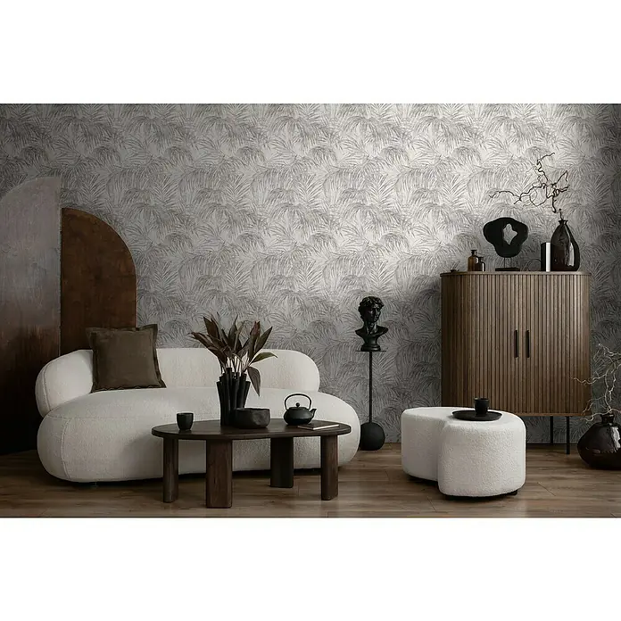 A.S. Création Michalsky Metropolis Vliestapete Farn - Weiß-Grau, Floral, 10,05 x 0,53 m - Elegantes Wohnzimmer mit beigem Sofa, Holztisch und passendem Schrank vor einer Tapete mit Blättermuster.