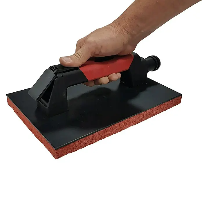 Heka Saugheber - Passend für: Industriesauger ab 1200 W, Tragkraft: 40 kg - Nahaufnahme einer Hand, die eine schwarze Fliesenfugenbürste mit rotem Schwammgriff hält.