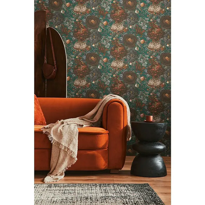 A.S. Création Michalsky Metropolis Vliestapete Blüten - Grün-Grau-Orange, Floral, 10,05 x 0,53 m - Elegantes Wohnzimmer mit einem orangefarbenen Sofa und einem kunstvollen schwarzen Beistelltisch vor einer floralen Tapete.