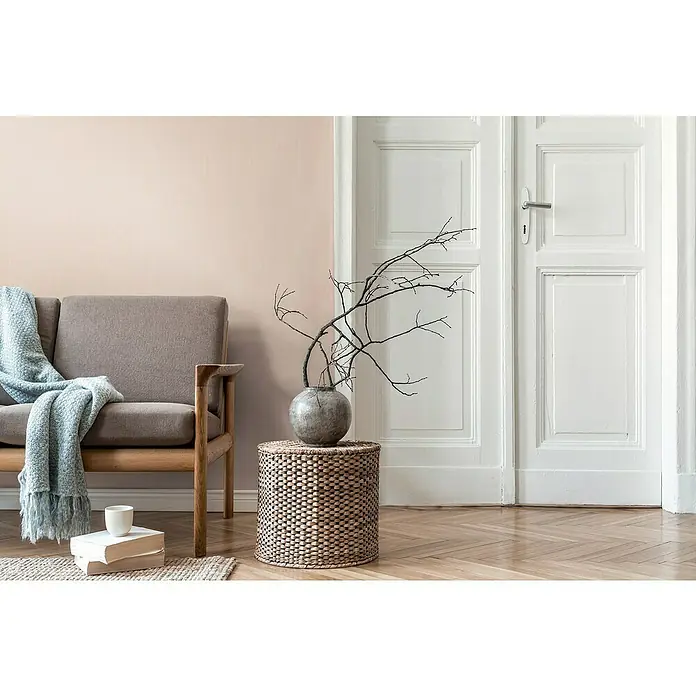 A.S. Création Daniel Hechter 7 Vliestapete - Beige I, Uni, 10,05 x 0,53 m - Einrichtungsszene mit einem stilvollen grauen Sofa, einer dekorativen Vase mit Ästen und einem Stapel Bücher, die eine ruhige und moderne Atmosphäre ausstrahlen.