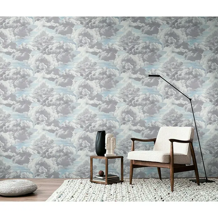 A.S. Création Michalsky Metropolis Vliestapete Wolken - Grau-Blau-Weiß, Sonstiges, 10,05 x 0,53 m - Ein gemütliches Wohnzimmer mit einem Sessel, einem Beistelltisch und einer Stehlampe vor einer Wolkentapete.