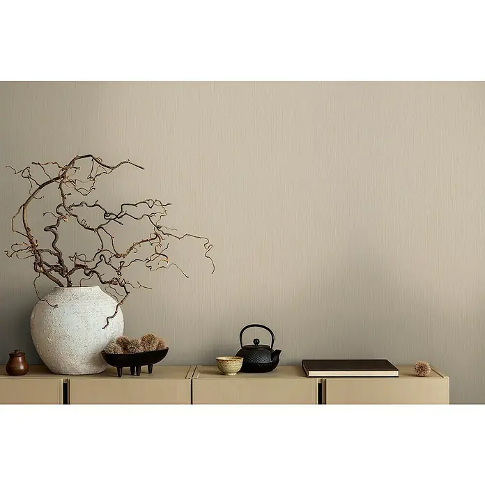 A.S. Création Michalsky Metropolis Vliestapete - Beigebraun, Uni, 10,05 x 0,53 m - Nahaufnahme eines minimalistischen Interieurs mit Keramikvase, Ästen und Tee-Set auf einem Sideboard vor einer strukturierten Wand.