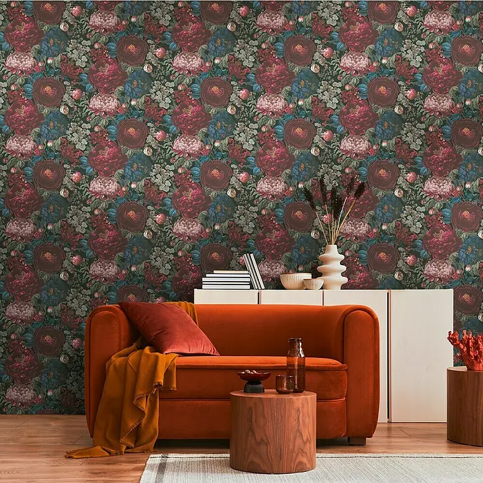 A.S. Création Metropolitan Stories Vliestapete Blüten - Rot-Blau-Schwarz, Floral, 10,05 x 0,53 m - Elegant eingerichtetes Wohnzimmer mit einem orangefarbenen Sofa, einem Beistelltisch und einer stilvollen Blumendekoration vor einer floralen Tapete.