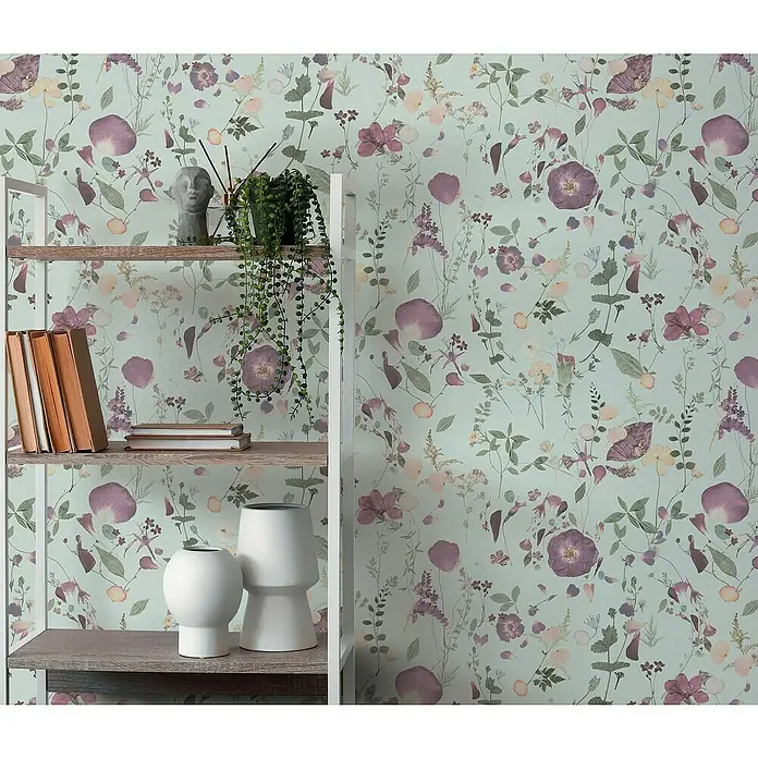 A.S. Création Pintwalls 2 Vliestapete Blumen - Grün-Violett-Gelb, Floral, 10,05 x 0,53 m - Dekoratives Regal mit Bücher, Vasen und Pflanzen vor einer floralen Tapete in sanften Farbtönen für ein gemütliches Ambiente.