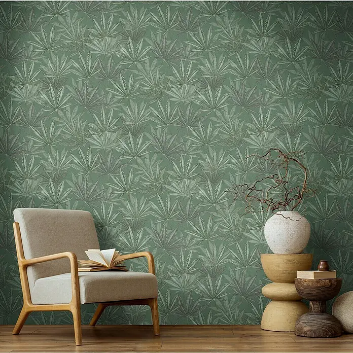 A.S. Création Michalsky Metropolis Vliestapete Hanfblätter - Grün, Floral, 10,05 x 0,53 m - Ein gemütliches Wohnzimmer mit einem Sessel und einem dekorativen Wandmuster.