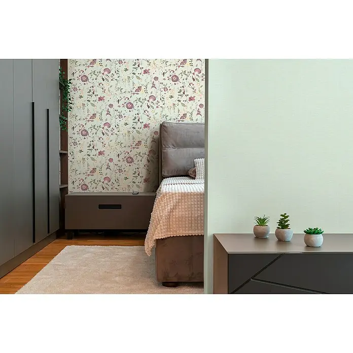 A.S. Création Pintwalls 2 Vliestapete Blumen - Grün-Violett-Gelb, Floral, 10,05 x 0,53 m - Ein gemütliches Schlafzimmer mit einem dekorativen Nachttisch, auf dem drei kleine Sukkulenten in Töpfen stehen, die das Zimmer beleben.