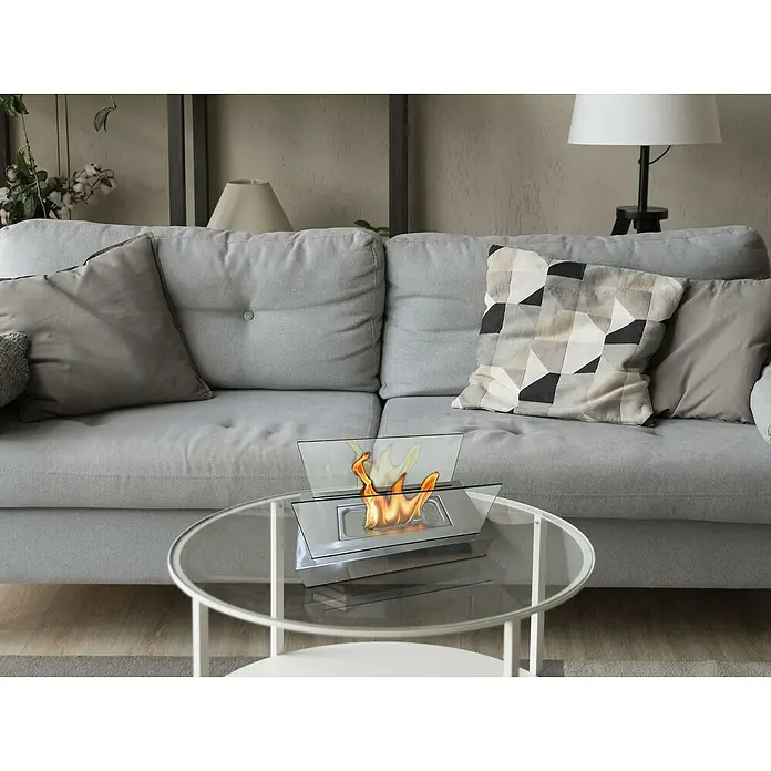 Purline Chimenea de bioetanol Algeiros - Acero inoxidable, Plateado - Primer plano de una chimenea de mesa de bioetanol sobre una mesa de centro con tapa de cristal frente a un sofá gris y decoración neutra.