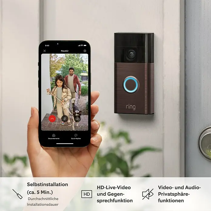 Ring Türklingel mit Kamera Battery Video Doorbell - Bronze, 2.560 x 1.440 Pixel, 2,3 x 6,19 x 12,65 cm - Nahaufnahme einer Person, die ein Smartphone mit einer Ring-Videotürklingel hält, die eine Live-Videoübertragung anzeigt.