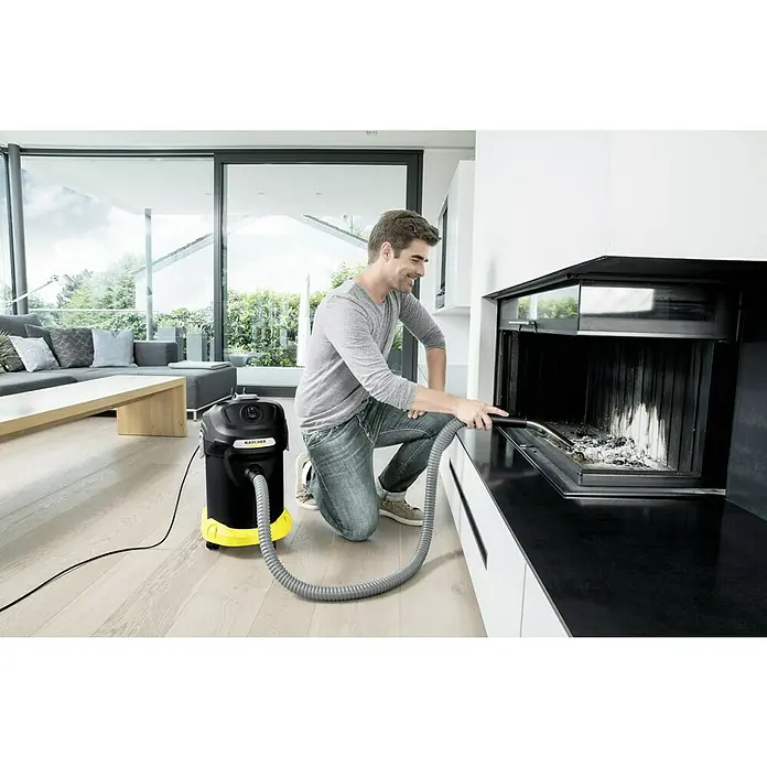 Kärcher Elektro-Aschesauger AD 4 Premium - 600 W, Behältervolumen: 17 l, Ohne Beutel - Mann reinigt einen Kamin mit einem Kärcher Aschesauger in einem hellen Wohnzimmer. Das Gerät ist schwarz mit gelben Akzenten.
