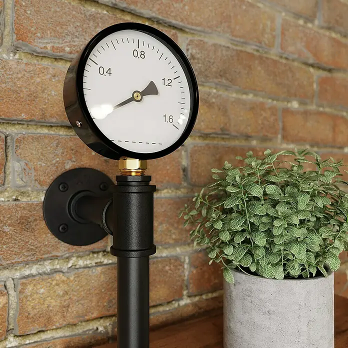 Walteco Rusticline Manometer - Stahl, Schwarz - Wandmontierter Manometer mit schwarzem Metallrohr und einem Zementtopf mit einer Pflanze auf einem Holztisch.