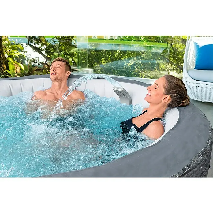Bestway Lay-Z-Spa Schwalldusche Xtras LED - Passend für: Bestway® AirJet™, AirJet Plus™ & UltraFit™ - Whirlpools - Ein Paar entspannt in einem aufblasbaren Whirlpool im Freien mit Massagedüsen und Wasserfallfunktion. Die graue Außenverkleidung fügt sich nahtlos in die natürliche Umgebung ein.