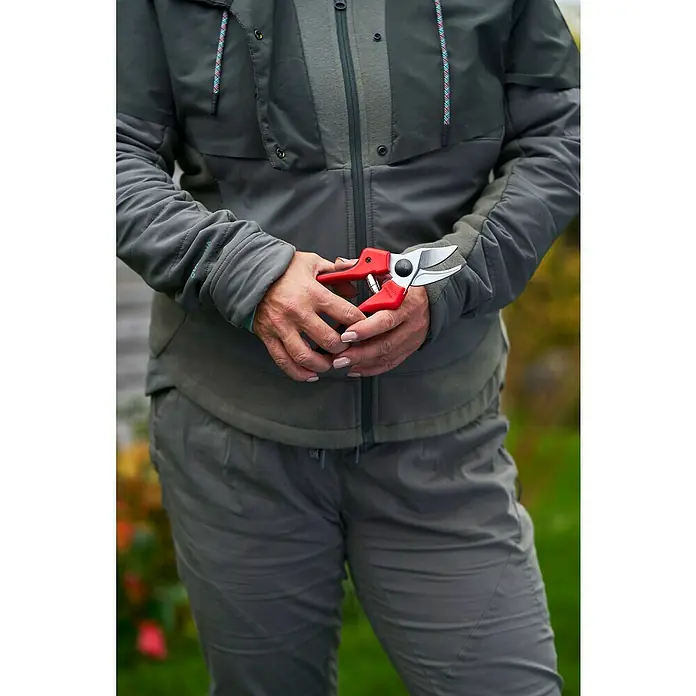 Felco Gartenschere 171M - Mittel - Max. Aststärke: 20 mm - Nahaufnahme einer Person mit einer roten Gartenschere in der Hand, bekleidet mit einer grünen Jacke und grauen Hosen.